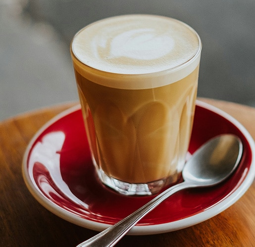 Glass latte med melkeskum på en rød skål